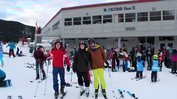 Eine Gruppe von Schülerinnen und Schülern der Delta Secondary School steht in Winterkleidung vor einer Skihütte auf einer verschneiten Piste.