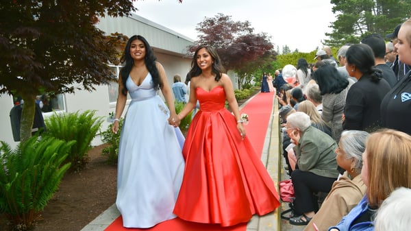 Zwei Schülerinnen der Delview Secondary School in eleganten Abendkleidern laufen auf dem roten Teppich im Garten.