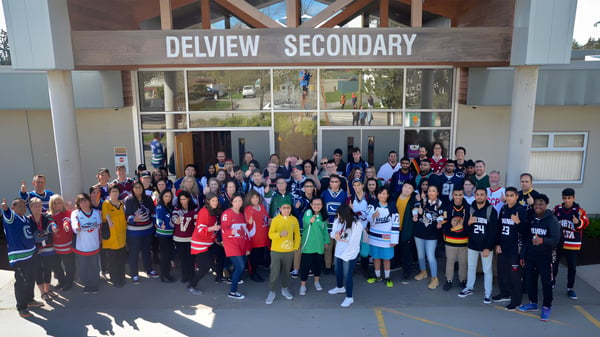 Eine große Gruppe von Schülerinnen und Schülern sowie Mitarbeiterinnen und Mitarbeitern versammelt sich vor dem Gebäude der Delview Secondary School.