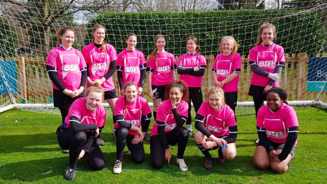 Eine Gruppe junger Fußballspielerinnen in pinken Trikots posiert auf dem Rasenfeld der Denefield School vor dem Tor.