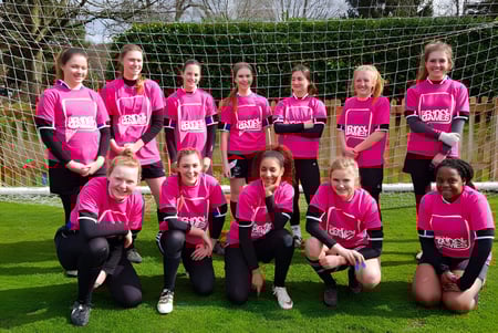 Eine Gruppe junger Fußballspielerinnen in pinken Trikots spielt auf dem Sportplatz der Denefield School.
