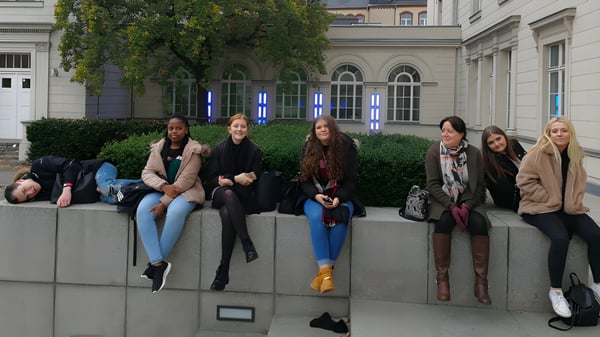 Eine Gruppe Schülerinnen sitzt vor einem Gebäude mit Rundbogenfenstern auf einer Steinmauer auf dem Gelände der Denefield School.