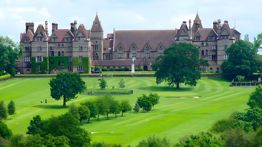 Ein mittelalterlich gestaltetes Schloss steht auf dem Gelände des Denstone College umgeben von gepflegtem Rasen und Bäumen.
