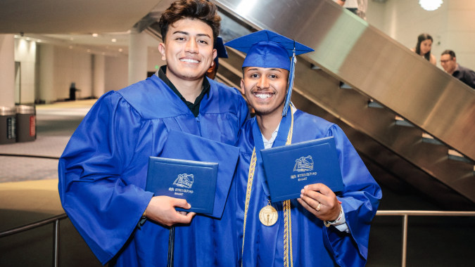 Zwei Schüler in blauen Abschlussroben halten ihre Diplome im Flur des Denver Public School Districts.