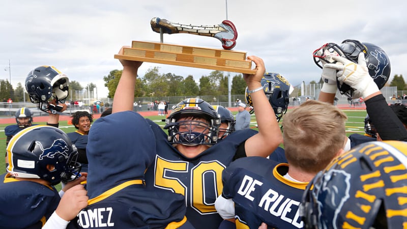Eine Gruppe junger Fußballspieler der Desert Sands Schools feiert auf dem Sportplatz mit einem Pokal.