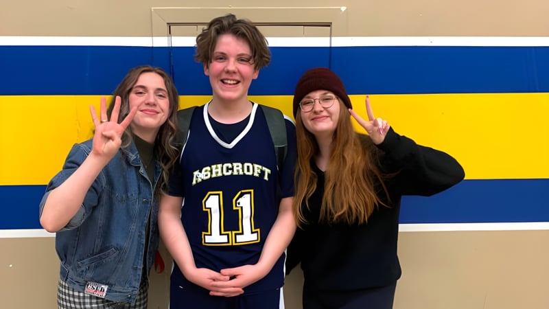 Drei Schülerinnen und Schüler der Desert Sands Schools posieren vor blau-gelbem Hintergrund mit verschiedenen Handgesten.