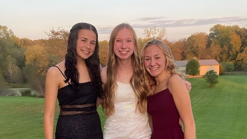 Drei Schülerinnen der Dexter High School posieren zusammen in formeller Kleidung vor einer grünen Wiese mit Bäumen.