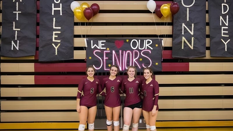 Vier Schülerinnen der Dexter High School stehen in einheitlichen Uniformen vor einem Banner mit dem Schriftzug We love our seniors.