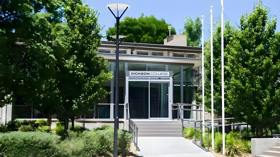 Das moderne Glas- und Stahlgebäude des Dickson College ist von grünen Bäumen und einem gepflasterten Weg umgeben.