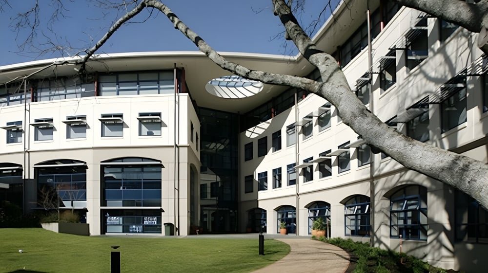 Das moderne mehrstöckige Gebäude der Diocesan School For Girls ist von einer Grünfläche mit Baumzweig im Vordergrund umgeben.