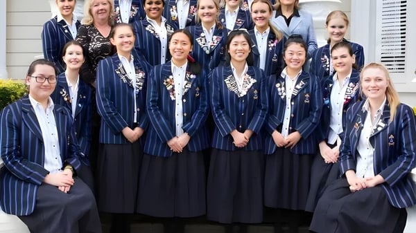 Eine Gruppe Schülerinnen der Diocesan School For Girls steht in Abschlusskleidung vor einem Gebäude mit weißen Säulen.