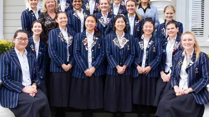 Eine Gruppe Schülerinnen der Diocesan School For Girls steht in einheitlichen Uniformen vor einem großen Gebäude mit Bögen.