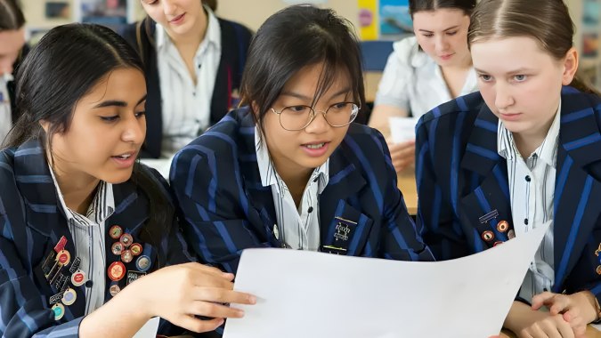 Schülerinnen der Diocesan School For Girls betrachten gemeinsam Dokumente im Klassenzimmer.
