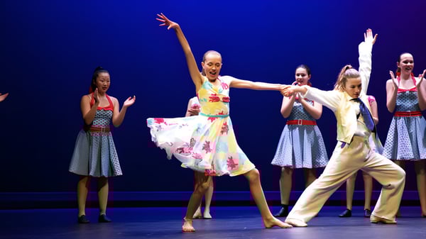 Eine Gruppe von Tänzerinnen führt auf der Bühne der Diocesan School For Girls eine farbenfrohe Tanzaufführung vor blauem Hintergrund auf.