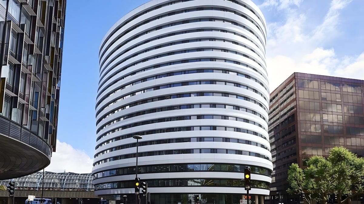 Das moderne Hochhaus des DLD College London mit mehreren Stockwerken und großen Fenstern ist vor einem klaren blauen Himmel zu sehen.