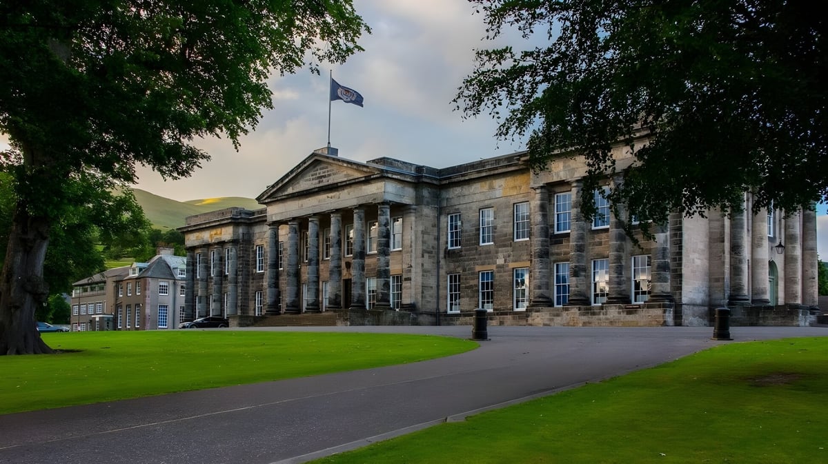 Das historisches Gebäude der Dollar Academy mit einer Säulenfassade steht umgeben von Grünflächen und einem gepflasterten Weg davor.