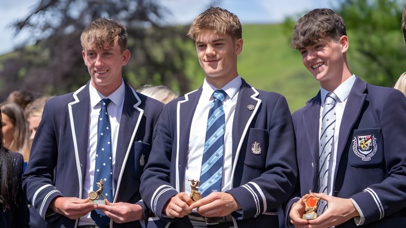 Drei Schüler in Schuluniformen stehen gemeinsam auf einer grünen Wiese im Freien auf dem Campus der Dollar Academy.