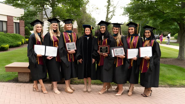Eine Gruppe Absolventinnen und Absolventen des Dominican College Galway steht im Freien auf einem gepflasterten Weg umgeben von grüner Vegetation.