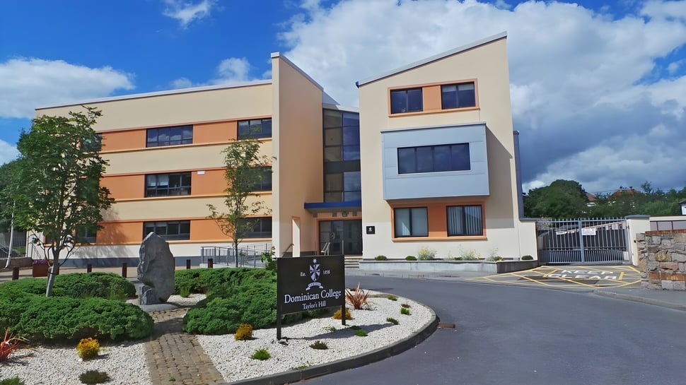 Das moderne Gebäude des Dominican College Galway mit angelegtem Vorgarten und einer Skulptur vor blauem Himmel.