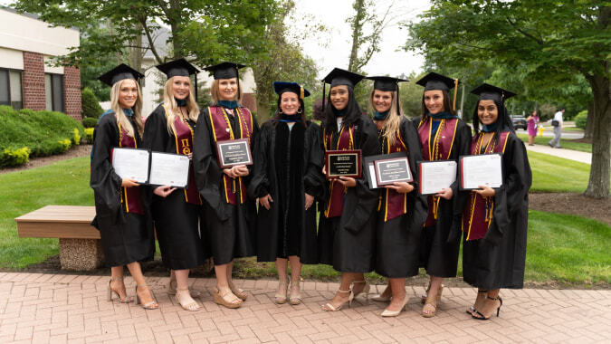 Eine Gruppe von Absolventinnen und Absolventen des Dominican College Galway steht mit Urkunden auf dem Campus vor Bäumen und Gebäuden.
