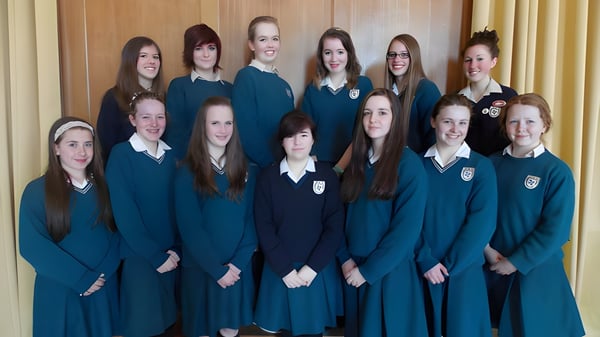 Eine Gruppe von Schülerinnen in einheitlicher Schuluniform steht vor einer holzverkleideten Wand auf dem Campus des Dominican College Wicklow.