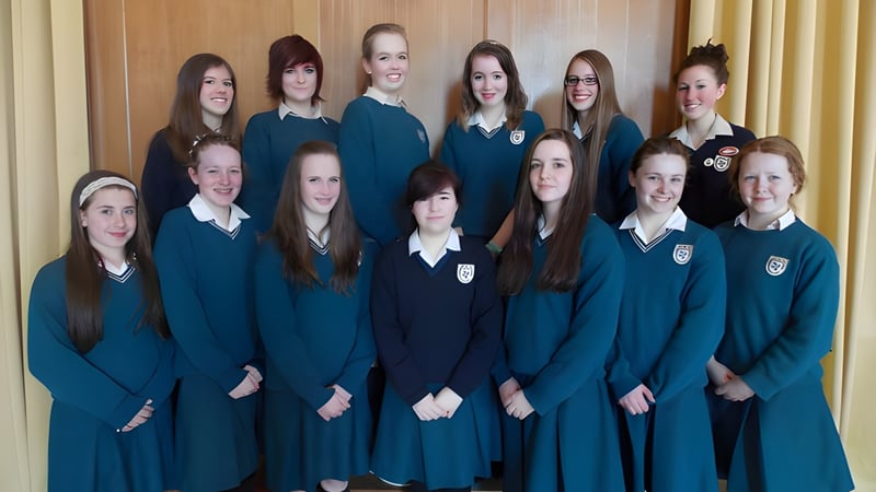 Eine Gruppe von Schülerinnen in einheitlicher Schuluniform steht vor einer holzverkleideten Wand auf dem Campus des Dominican College Wicklow.
