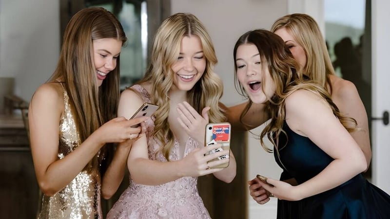 Vier Schülerinnen des Dominican College Sion Hill schauen gemeinsam lächelnd auf ein Smartphone in einem Innenraum.