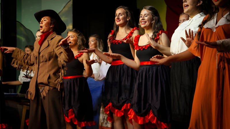 Eine Gruppe von weiblichen Schülerinnen des Dominican College Galway tritt in traditionellen Kleidern auf einer Bühne auf.