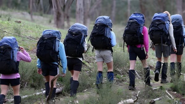 Eine Gruppe von Schülern des Dominican College Galway wandert mit großen Rucksäcken auf einem Waldweg.