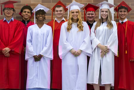 Eine Gruppe von Absolventinnen und Absolventen der Dominion Academy of Dayton steht vor einer Backsteinwand und feiert ihren Abschluss.