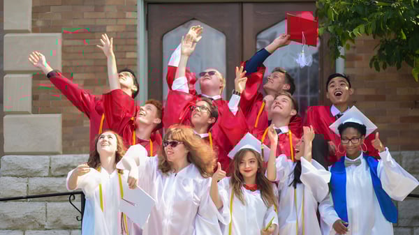 Eine Gruppe von Absolventen der Dominion Academy of Dayton feiert vor einem Backsteingebäude ihren Abschluss.