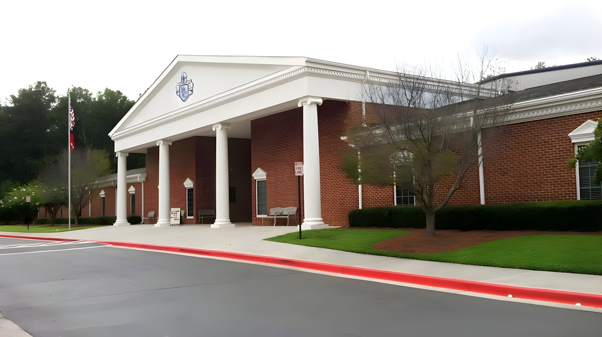 Das Backsteingebäude der Dominion Christian School mit einer Säulenveranda steht vor einem grünen Rasen und Bäumen.