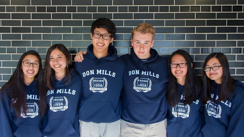 Eine Gruppe von Schülern des Don Mills Collegiate Institute trägt blaue Hoodies mit dem Schriftzug Don Mills vor einer gekachelten Wand.
