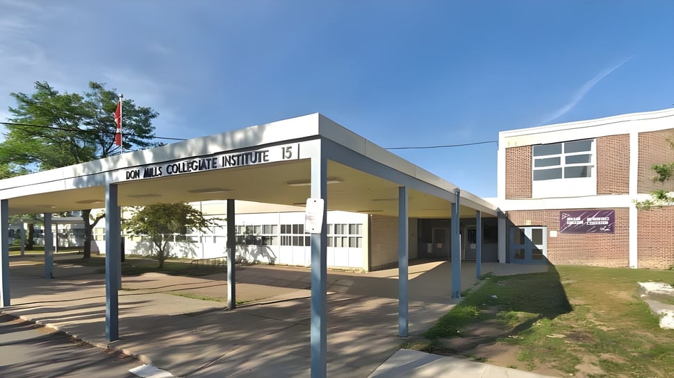 Das moderne mehrstöckige Gebäude des Don Mills Collegiate Institute mit überdachtem Weg und umgeben von Bäumen unter klarem Himmel.