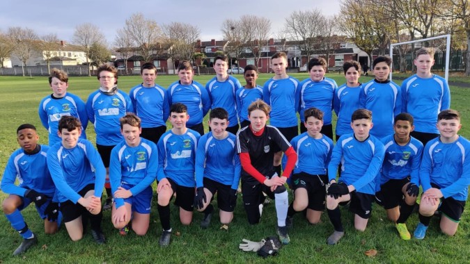 Eine Gruppe von Schülerinnen und Schülern der Donahies Community School posiert im blauen Trikot für ein Mannschaftsfoto auf dem Fußballfeld.