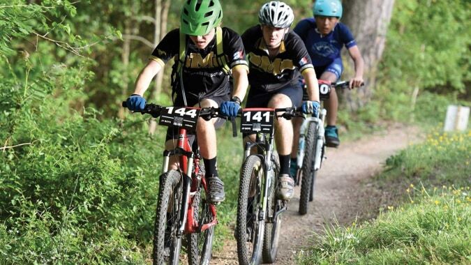 Drei Schülerinnen und Schüler der Donahies Community School fahren Mountainbikes auf einem Waldweg.