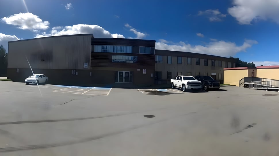 Das moderne mehrstöckige Gebäude mit Glasfassade auf dem Campus der Dorset Collegiate ist von einem gepflasterten Parkplatz umgeben.