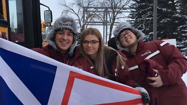 Drei Schülerinnen des Dorset Collegiate tragen identische rote Hoodies und halten gemeinsam ein großes Banner.