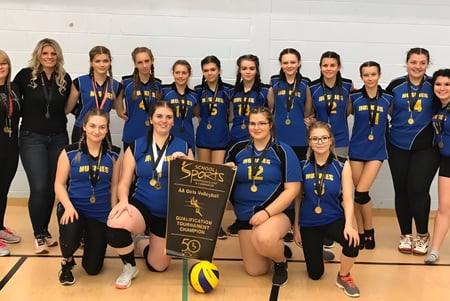 Eine Gruppe von Volleyballspielerinnen der Dorset Collegiate steht gemeinsam in einer Sporthalle und hält einen Pokal.