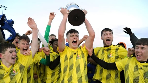 Eine Gruppe junger Fußballspieler feiert mit einem Pokal auf dem Spielfeld der Douglas Community School.
