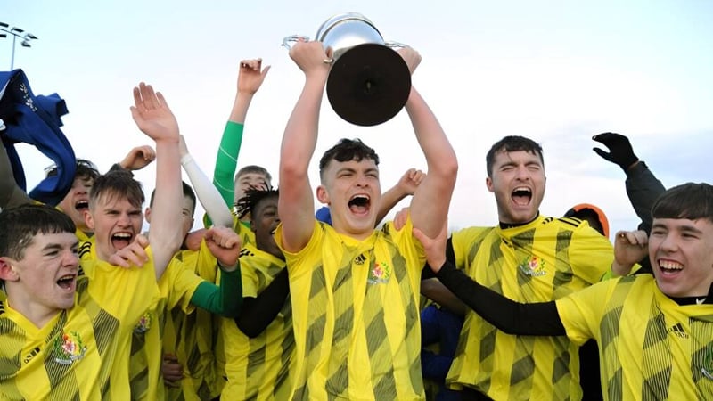 Eine Gruppe junger Fußballspieler feiert mit einem Pokal auf dem Spielfeld der Douglas Community School.