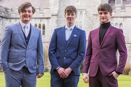 Drei Schüler in formeller Kleidung stehen vor einem historischen Gebäude auf dem Gelände der Douglas Community School.
