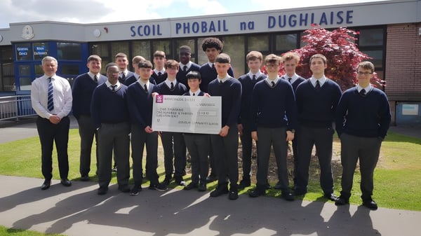 Schüler der Douglas Community School stehen in Schuluniformen vor dem Schulgebäude und halten einen großen Scheck.