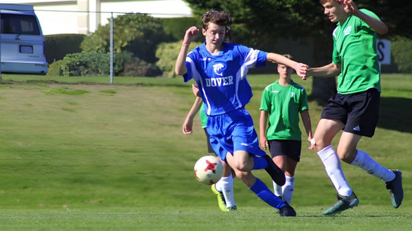 Zwei Schülerinnen der Dover Bay Secondary School spielen Fußball auf einem grünen Spielfeld vor einem Tor.