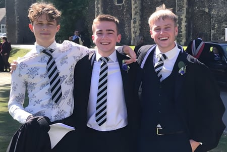 Drei Schüler in Schuluniformen stehen draußen auf dem Campus des Dover College und lachen.