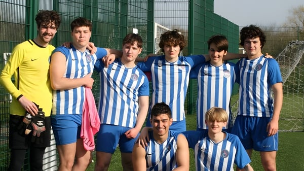 Eine Gruppe junger Fußballspieler steht vor einem grünen Drahtzaun auf dem Gelände von D'Overbroeck's College.