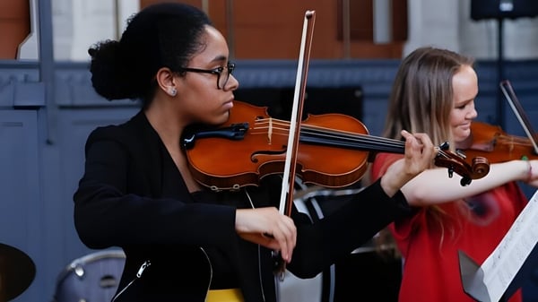 Ein junger Mann im schwarzen Anzug spielt Geige neben einer jungen Frau im roten Kleid während einer Aufführung am D'Overbroeck's College.