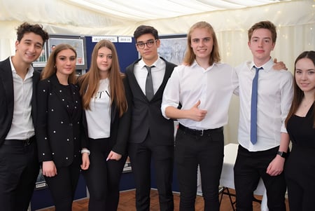 Eine Gruppe Schüler in formeller Kleidung posiert vor einem weißen Zelt auf dem Campus von D'Overbroecks College.