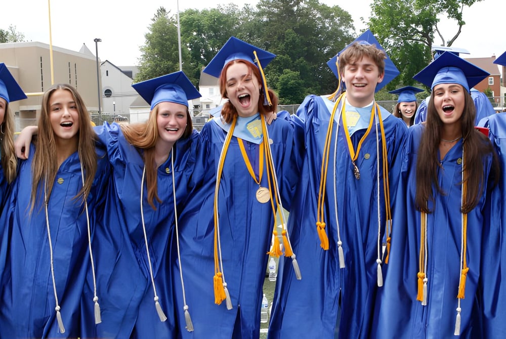 Eine Gruppe von Absolventen des Downingtown Area School District steht im Freien in blauen und gelben Abschlussgewändern zusammen.