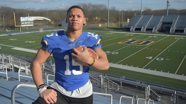 Eine Person in blauem Sporttrikot steht auf dem Fußballfeld des Downingtown Area School District mit Stadion und Tribünen im Hintergrund.